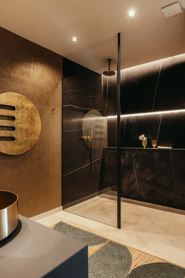 Badezimmer mit goldener Wandscheibe, schwarzem Marmor und indirekter Beleuchtung