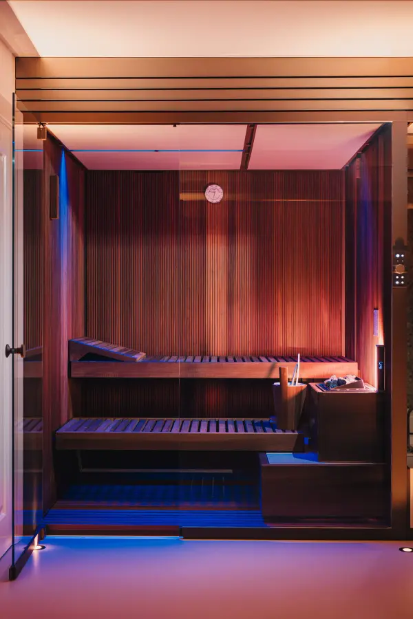 Sauna mit Holzbänken und blau-rotem Farblicht hinter Glasfront