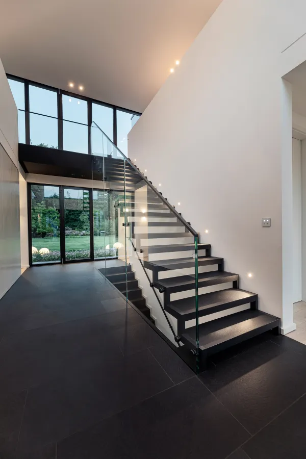 Schwebende schwarze Treppe mit Glasgeländer vor einer hohen Fensterfront
