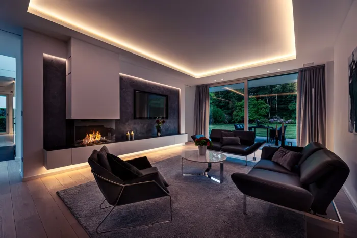Wohnzimmer mit Kamin, indirekt beleuchteter Decke, Ledersesseln und Blick in den Garten